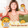 A smiling girl holds a yellow crochet taco doll with a positive message card and a taco in her hand.