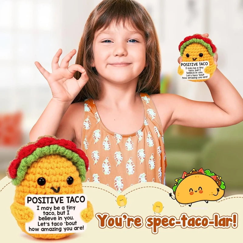 A smiling girl holds a yellow crochet taco doll with a positive message card and a taco in her hand.
