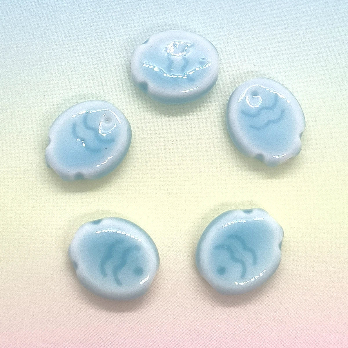 Five handcrafted ceramic fish beads in varying shades of light blue arranged in a star pattern.