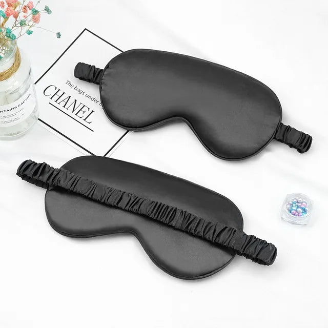 A black silk sleep mask is shown on a white background next to a Chanel branded card.