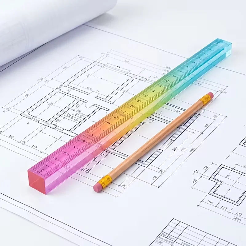 A colorful geometric cube drawing tool with a straight edge is shown next to technical drawings on paper.