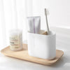 A white bamboo bathroom organizer set holding a toothbrush and a tube of cream.