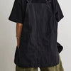 A person wearing a black waterproof work apron over a dark shirt and olive green shorts.