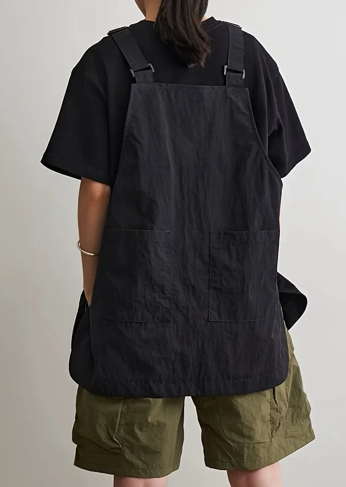 A person wearing a black waterproof work apron over a dark shirt and olive green shorts.