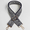 A dark navy and white paisley jacquard bag strap with a gold buckle and leather accents.