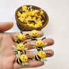 A hand holds several yellow 3D bee silicone beads and a bowl full of similar bees for jewelry making