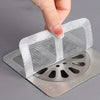 A hand is placing a disposable drain hair catcher sticker onto a metal drain grate.