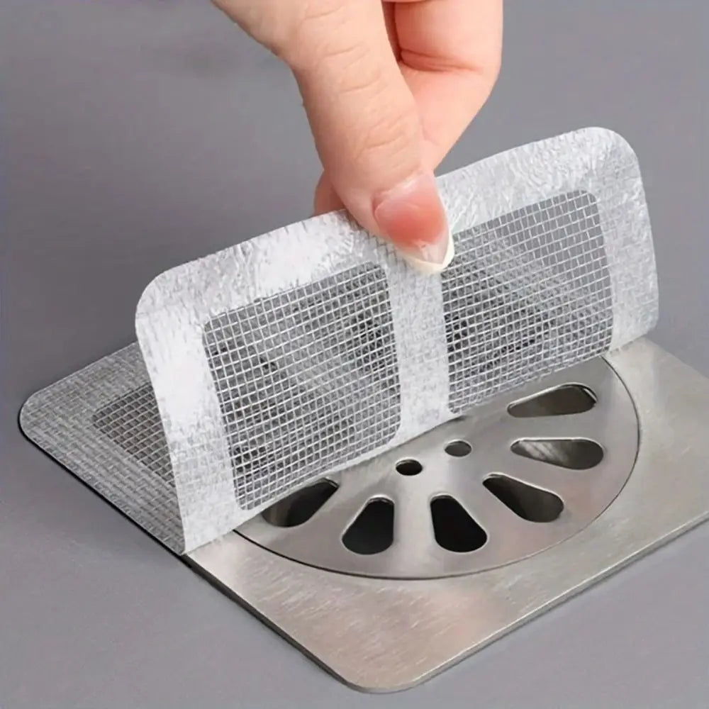 A hand is placing a disposable drain hair catcher sticker onto a metal drain grate.