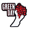 A black and white pin featuring the text GREEN DAY and a red fist design.