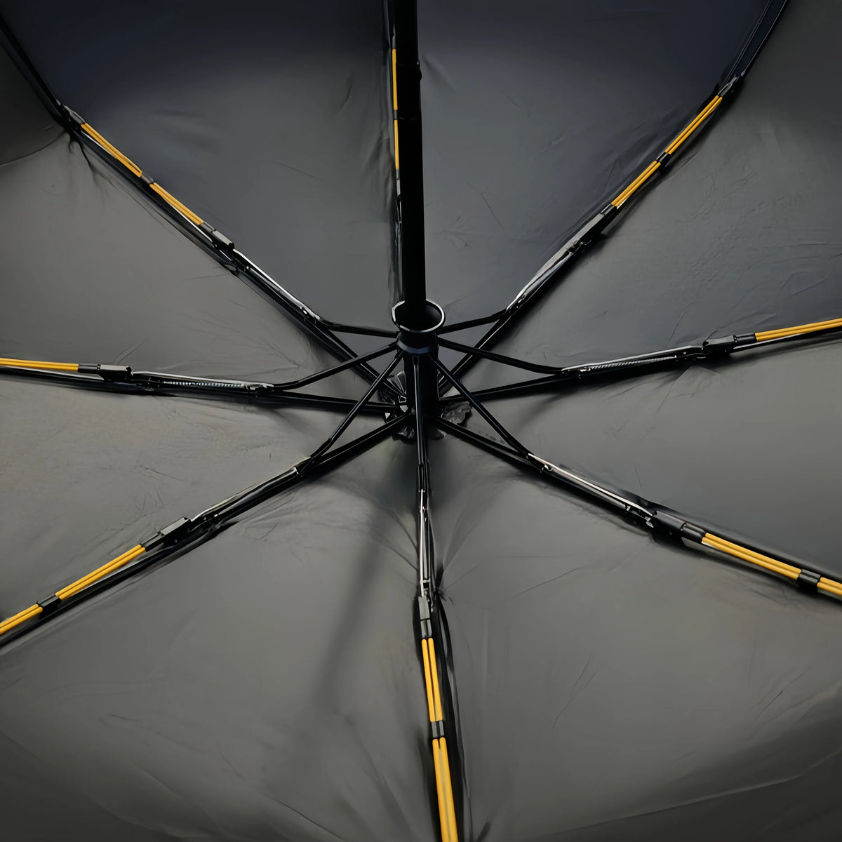 A black windproof umbrella with yellow accents is shown open, displaying its spokes and canopy.