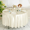 A round table set for an event featuring a cream satin tablecloth, white plates, silverware, and floral centerpieces.