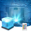 A blue glowing cube projector light illuminating water patterns and a remote control.