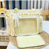 A yellow transparent shoulder bag with white lace trim resting on a woven mat.