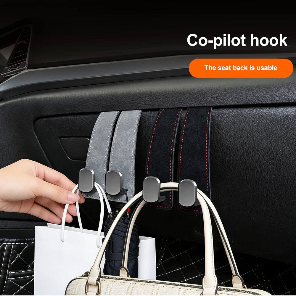 A hand is shown using a co-pilot hook to hang a white handbag from the seat back of a car.