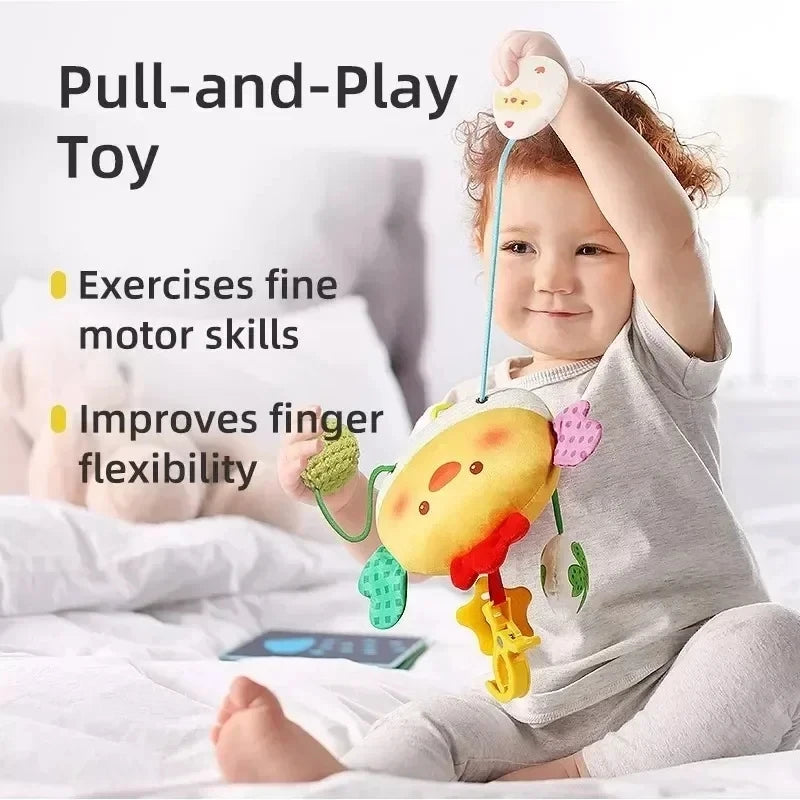 A baby is holding a yellow and pink sensory toy with a hanging crab design, used for fine motor skill exercises.