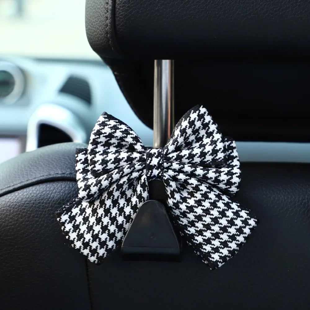 A black and white checkered bow-shaped car seat back hook with storage mounted on a vehicle interior.