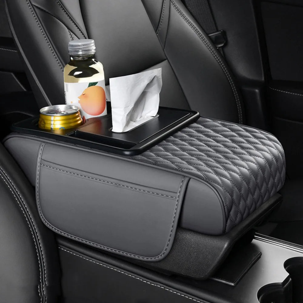 A black car armrest cushion with diamond stitching, featuring storage and cup holders, sits on a dark leather seat.