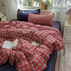 A red and black plaid bedding set featuring a duvet cover, flat sheet, and pillowcases displayed on a dark blue surface.
