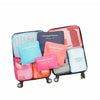 A set of six colorful laundry pouches or packing cubes displayed on a black stand.