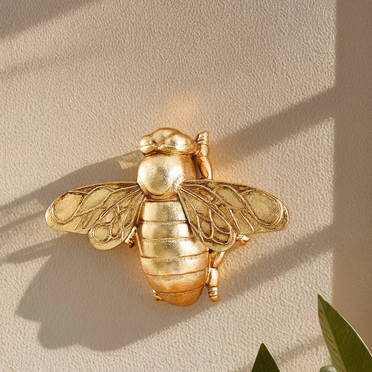 Golden bee-shaped resin wall decor mounted on a light beige wall.