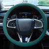 A close-up view of a dark steering wheel covered with a green silicone anti-slip grip.
