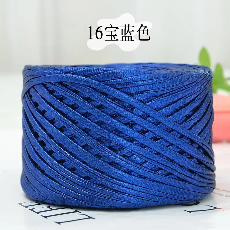 A spool of metallic blue flat ribbon yarn for crochet and knitting, showing its texture and color.