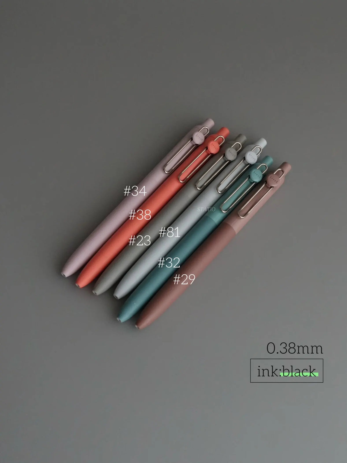 A collection of Uni ZENTO Quick-Dry Gel Pens in various shades of pink, red, and blue are arranged diagonally on a gray surfa