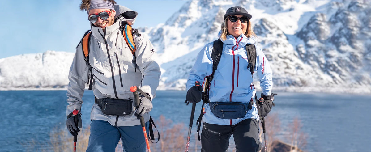 Two women hiking in snowy mountains with backpacks and fanny packs