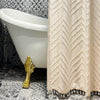A beige bohemian floral cutout tassel shower curtain hangs next to a white bathtub and gold fixture on patterned tile floor.