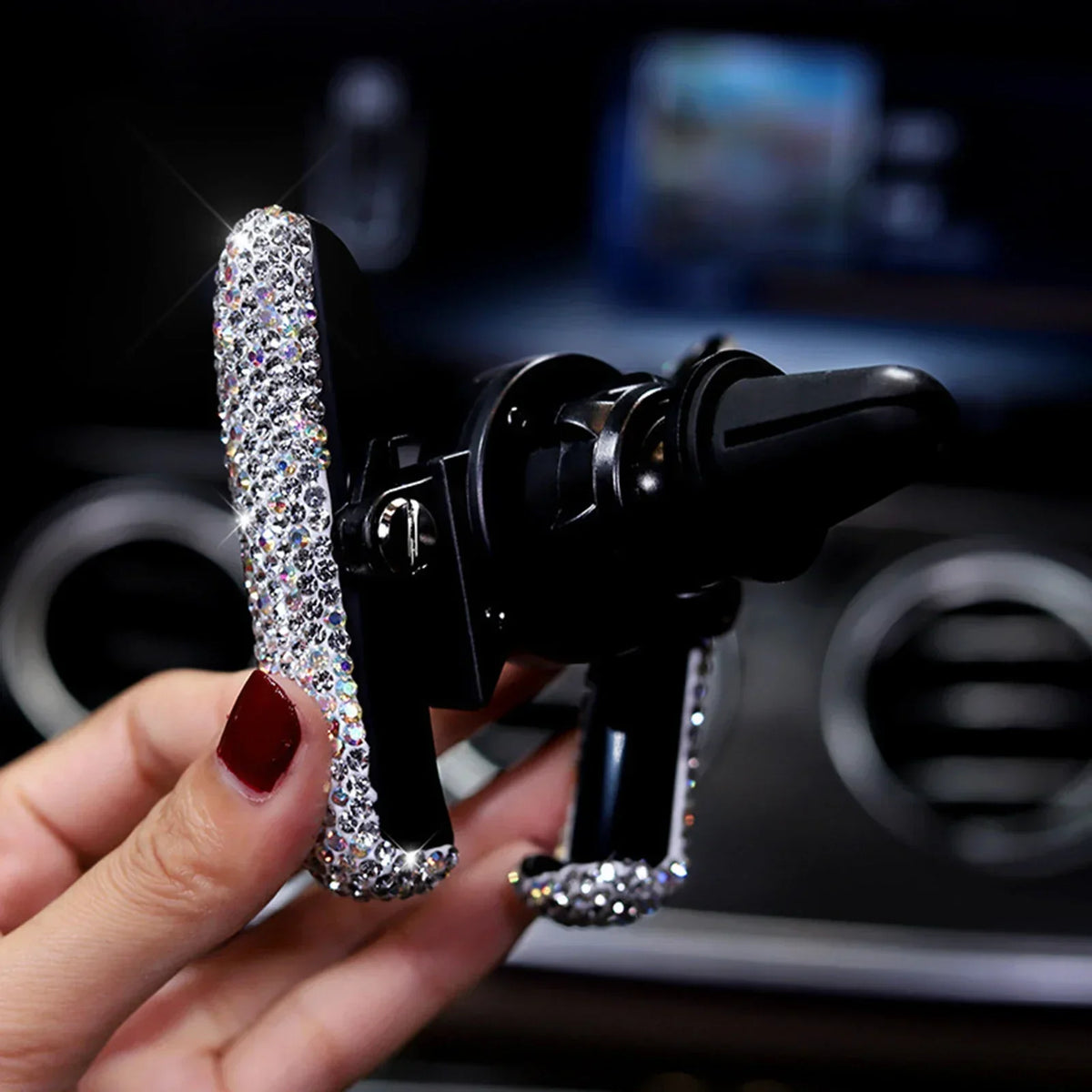 A hand holds a black crystal air vent car phone holder device.