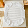 White waterproof fitted mattress protector with quilted texture placed on a light-colored surface.