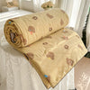 A tan quilt with a pastoral print featuring small brown teddy bears and yellow accents, rolled up on a white bed.