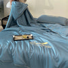 A teal ultra-soft cooling comforter with embroidery is displayed on a bed, featuring a hood and a decorative pillow.