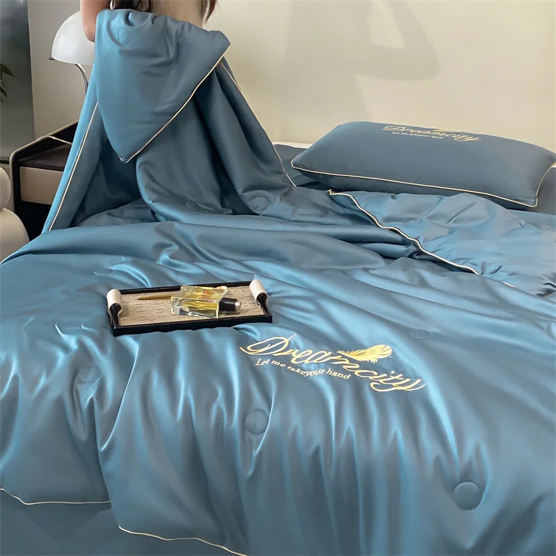 A teal ultra-soft cooling comforter with embroidery is displayed on a bed, featuring a hood and a decorative pillow.