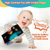 A baby is smiling while holding a high contrast toy with crinkle pages for auditory development.
