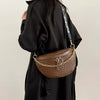 A brown woven pattern waist bag with a gold chain strap is shown being held by a person wearing a black coat.