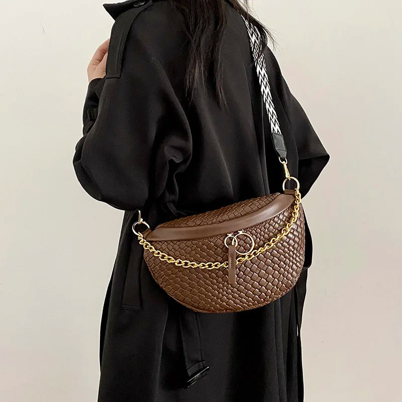 A brown woven pattern waist bag with a gold chain strap is shown being held by a person wearing a black coat.