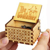 A wooden music box with a lid featuring the text The Godfather is held in a hand.