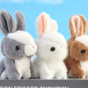 A set of three mini plush bunny toys with gray, white, and brown fur standing on a gray surface.