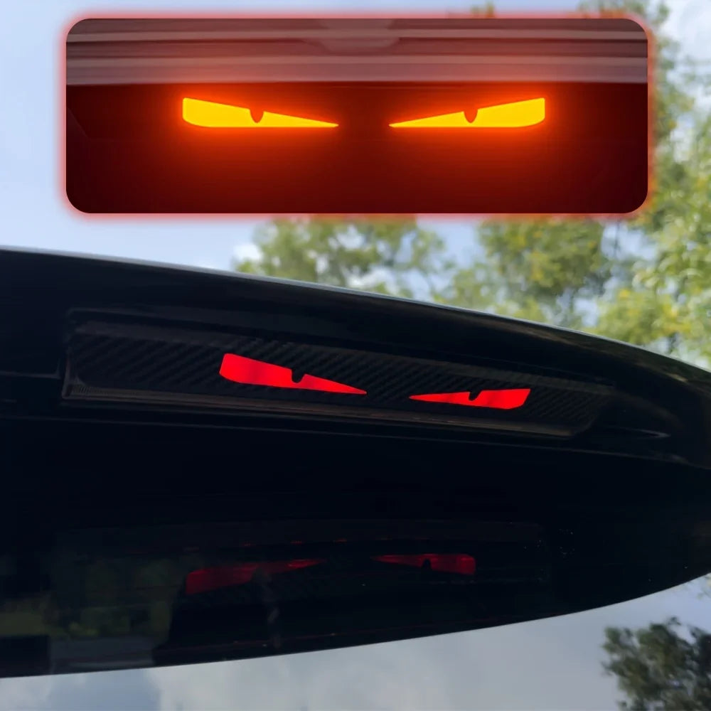 Close-up of a red brake light decal featuring an angry devil eye design on a black car.