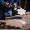 A person is using a dark-handled sanding block to sand a piece of light wood on a wooden surface.
