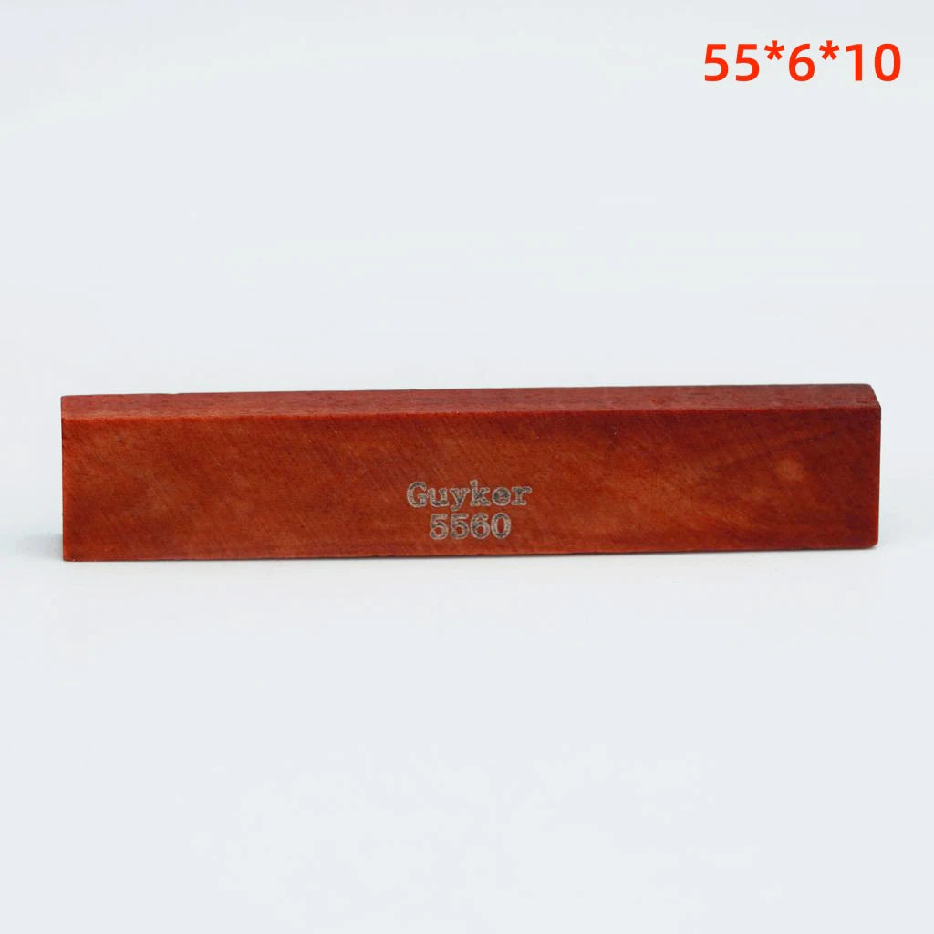 A rectangular piece of reddish-brown wood labeled Guykor 5560, used as an acoustic guitar bridge saddle.