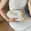 A woman holds a white sequin beaded chain shoulder clutch bag against a white dress.