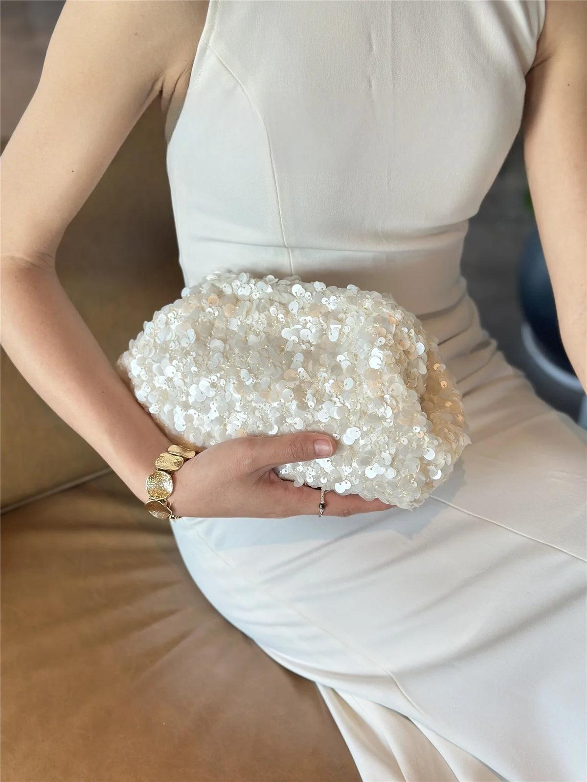A woman holds a white sequin beaded chain shoulder clutch bag against a white dress.