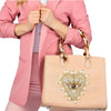 A woman wearing a pink blazer is holding a light pink handbag with gold beaded rhinestone patches.