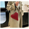 A woman holds a heart-shaped red PU coin purse with a black strap against a light beige trench coat.