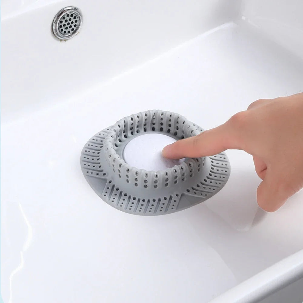 A hand is placing a silicone drain hair catcher into a white bathtub or sink, showing the mesh design.