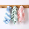 Three folded microfiber kitchen cleaning cloths in blue, green, and pink hanging on a wooden rack.