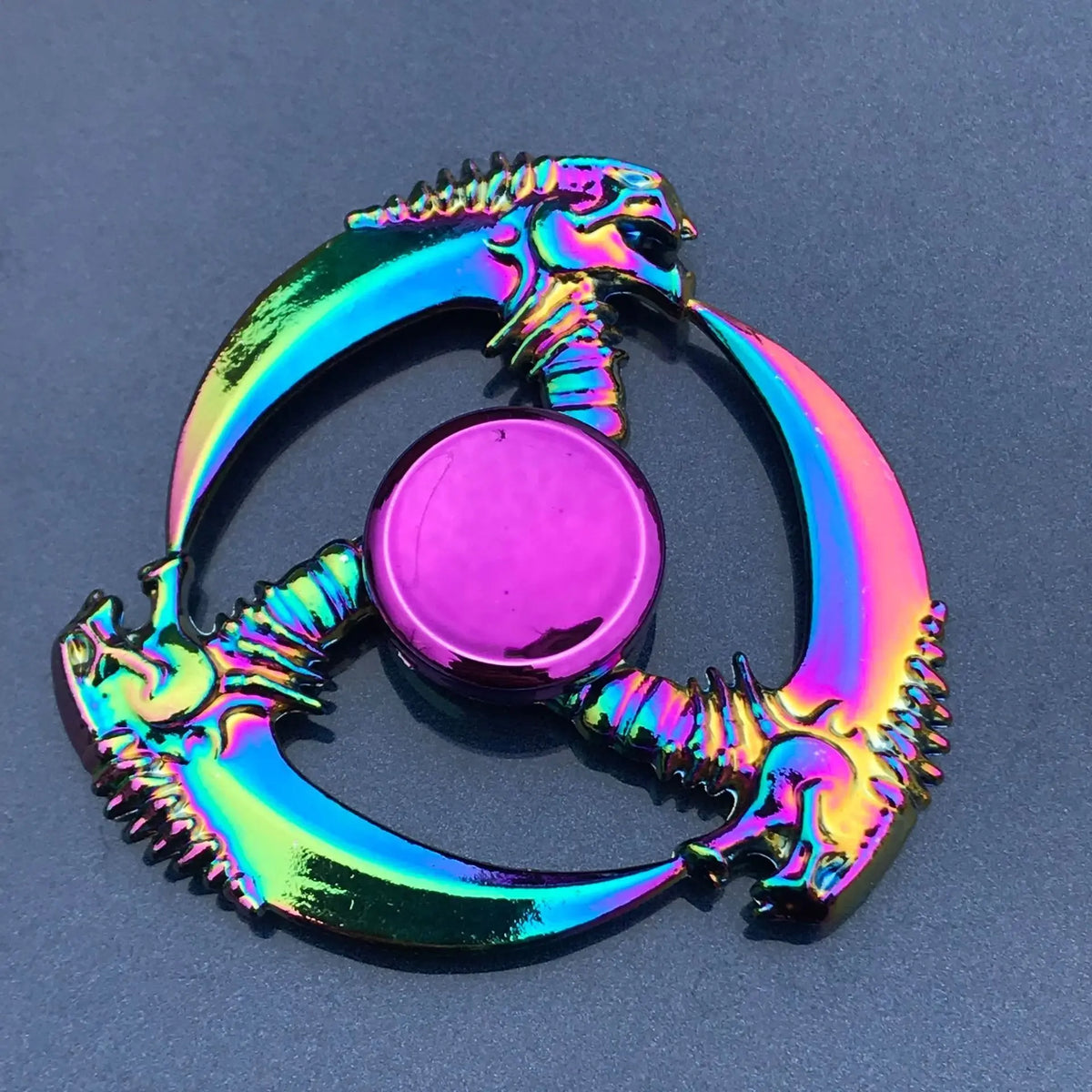 Un spinner anti-stress en alliage de zinc coloré, en forme de dragon ou de créature mythique avec un centre rose.