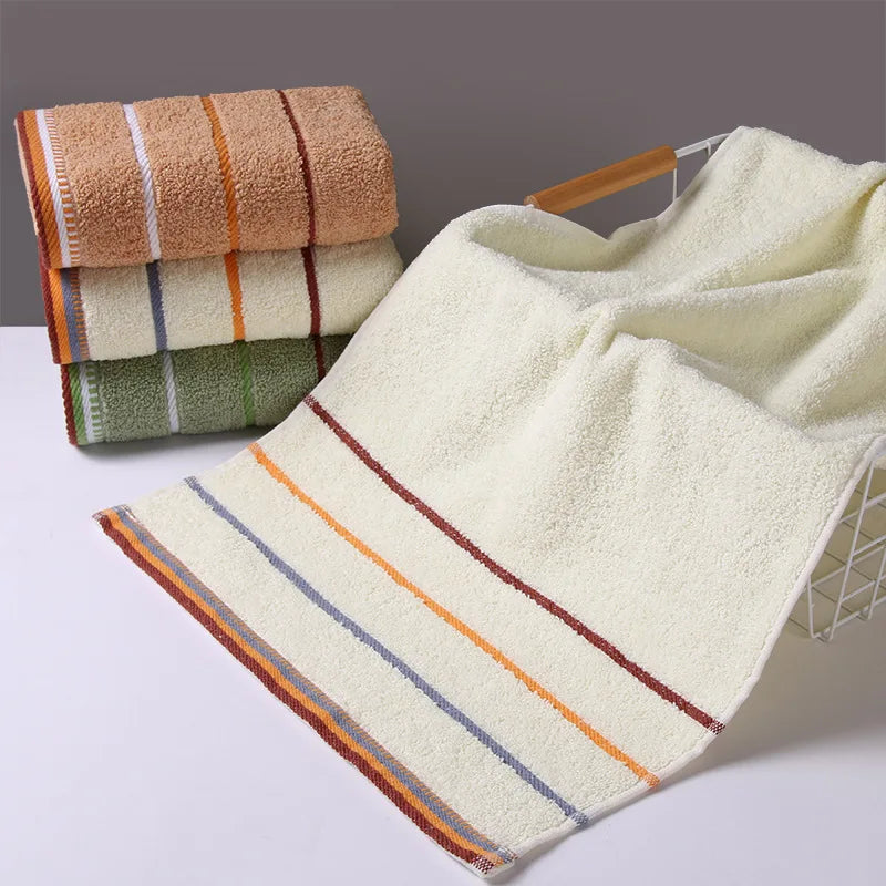 A set of stacked bath towels in beige, green, and striped colors, with a folded towel displayed on a white surface.